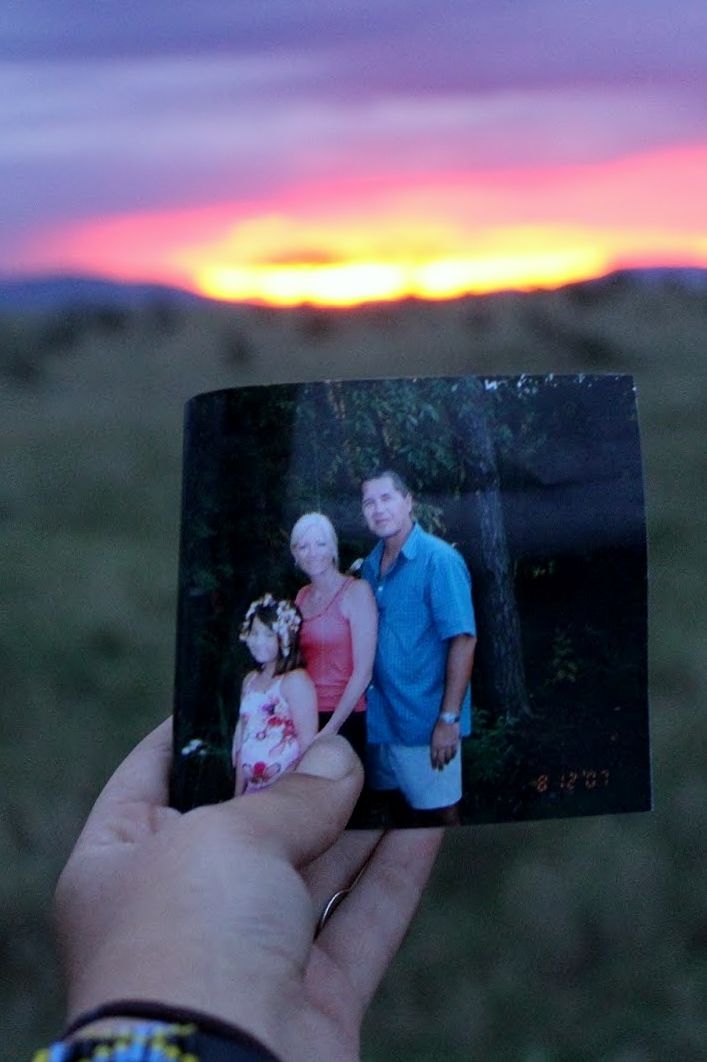 A safari visitor holds a family photo in front of a sunset.