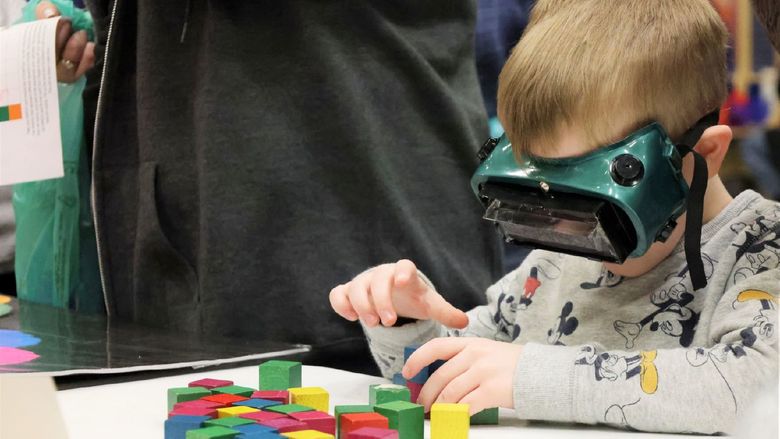 A boy wearing a VR headset stacks blocks at an activity table at the Penn State Behrend STEAM fair.