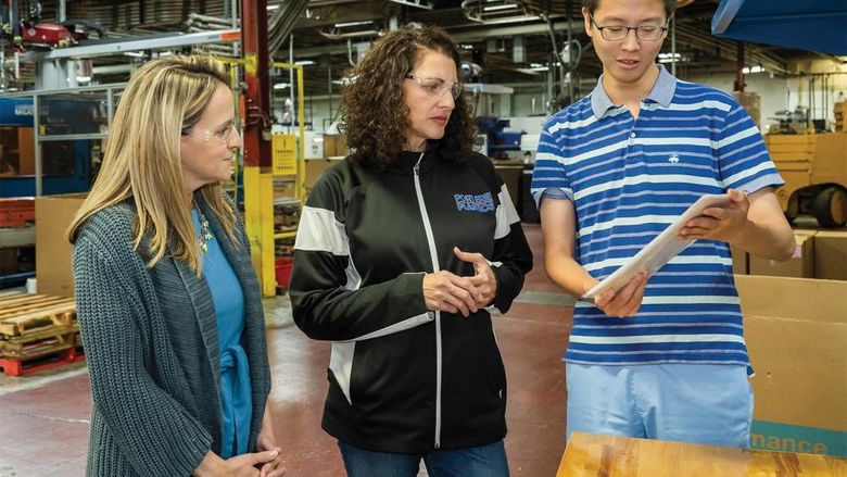 A Penn State Behrend student shows a sign he translated to a professor and a corporate executive during a visit to the shop floor at Port Erie Plastics.