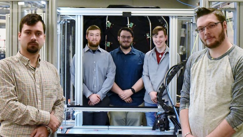 Five students pose near a large-scale 3D printer in Penn State Behrend's Innovation Commons lab.