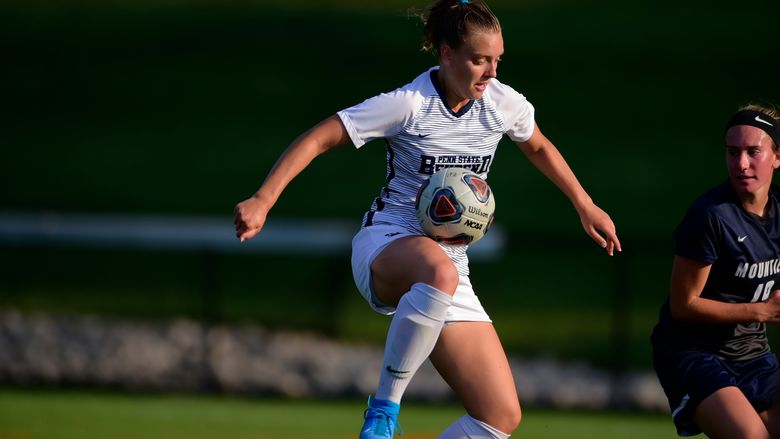 A female Penn State Behrend soccer player juggles the ball off her knee during a game.
