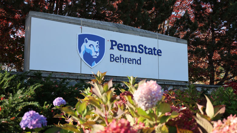 The entrance sign to Penn State Behrend with lion shield and flowers