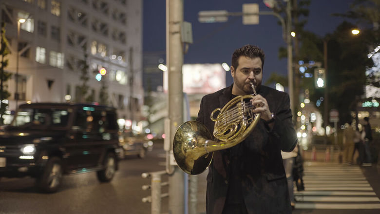 A horn player holds his instrument while walking in the street.