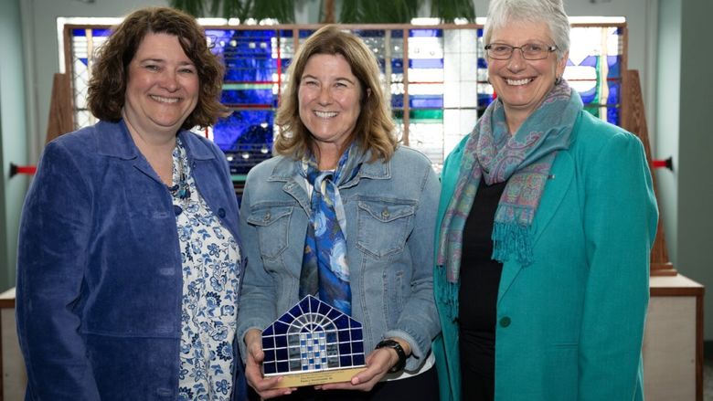 Women's Engagement Council board members Melanie Ford and Priscilla Hamilton present the Mary Behrend Impact Award to Paula J. Dombrowski.