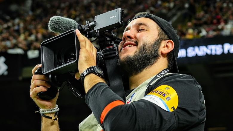 Josh Sige looks through a video camera on the sideline during an NFL game.
