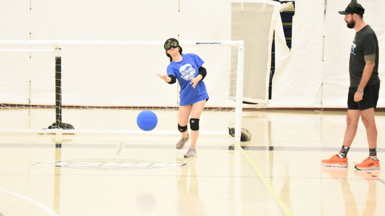 A blind player wearing ski goggles rolls a ball during a game of goalball.