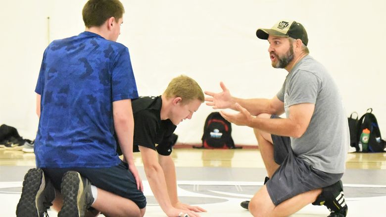 A wrestling coach instructs two blind junior athletes on a mat in Penn State Behrend's Junker Center.