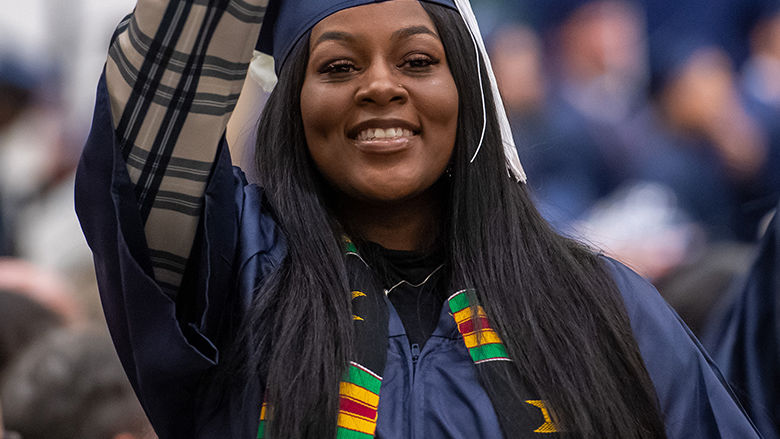 Black female student waves at commencement.