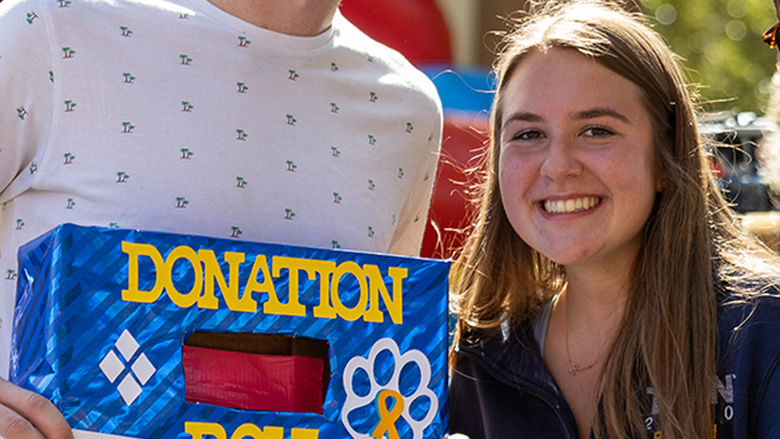 Male and female student hold donation box and sign for Penn State THON.