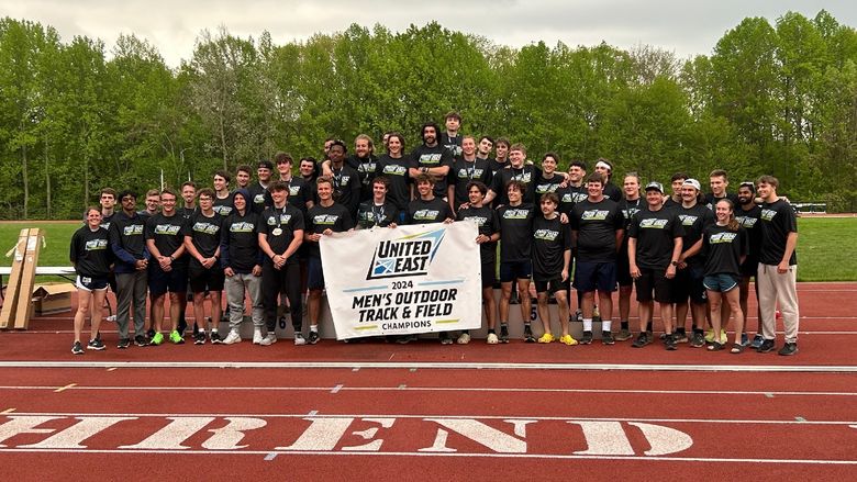 The Penn State Behrend men's track and field team celebrates with the United East championship banner.