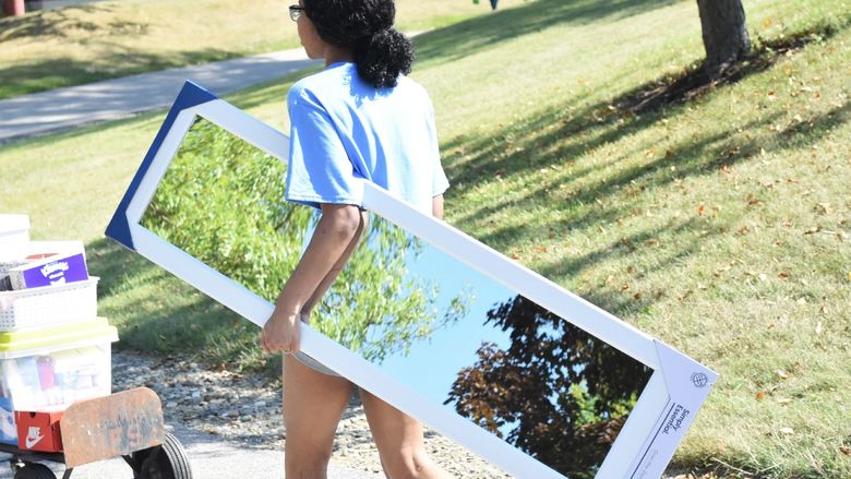 A female student carries a mirror into a residence hall during Penn State Behrend's move-in day.