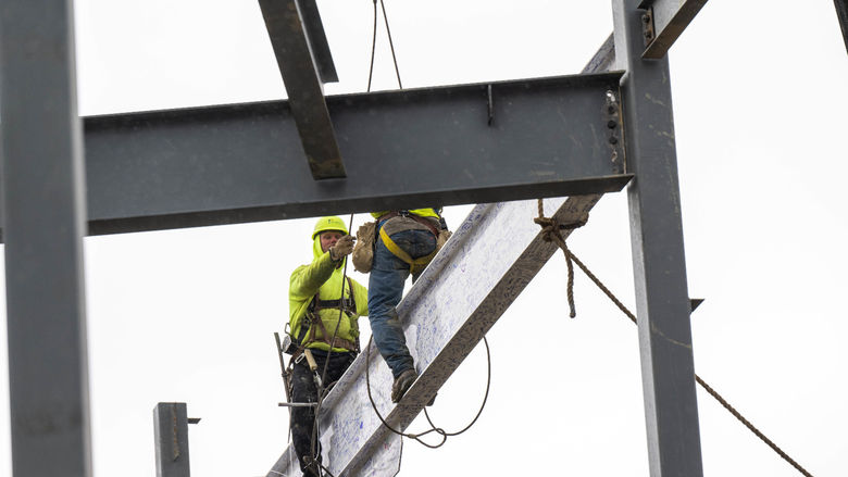 Two steelworkers set a beam in place at the site of Penn State Behrend's new Erie Hall.