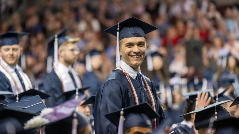 A student stands and smiles during Penn State Behrend's spring 2022 commencement program.
