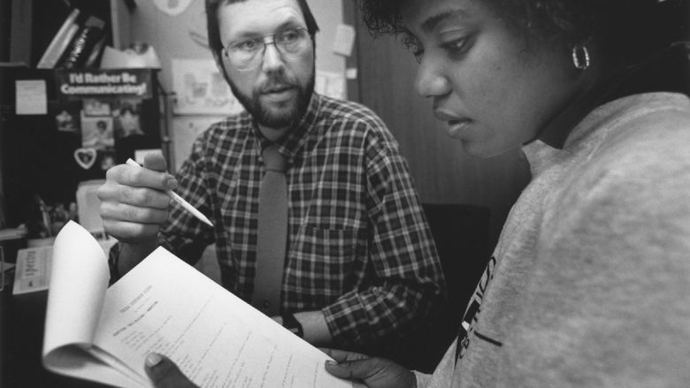 A black-and-white photo of Rod Troester, associate professor emeritus of speech communication, in an office with a student.