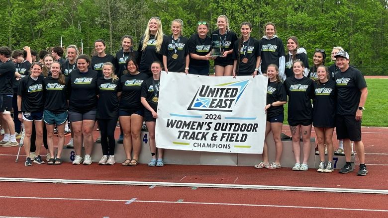The Penn State Behrend women's track and field team celebrates with the United East championship banner.
