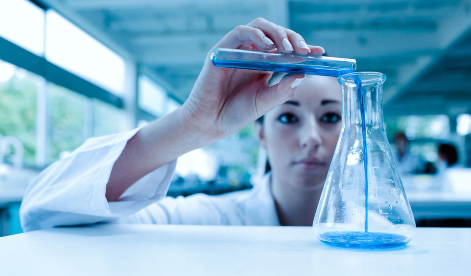 A laboratory researcher pours blue liquid in a container.