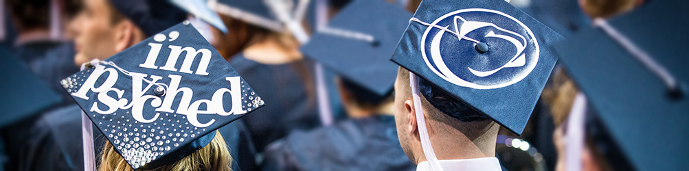 Two graduates wear custom mortarboards with "I'm Psyched" and a Penn State logo