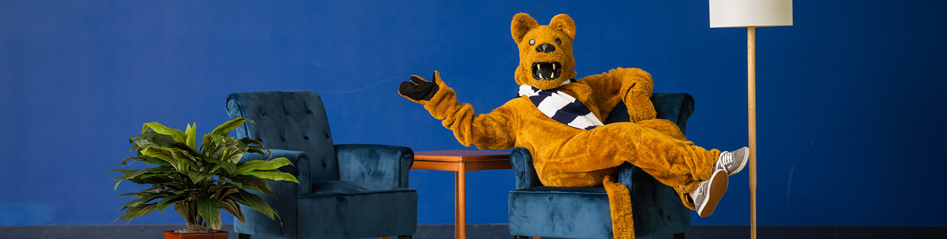 Lion mascot sitting in one of two blue armchairs on a stage
