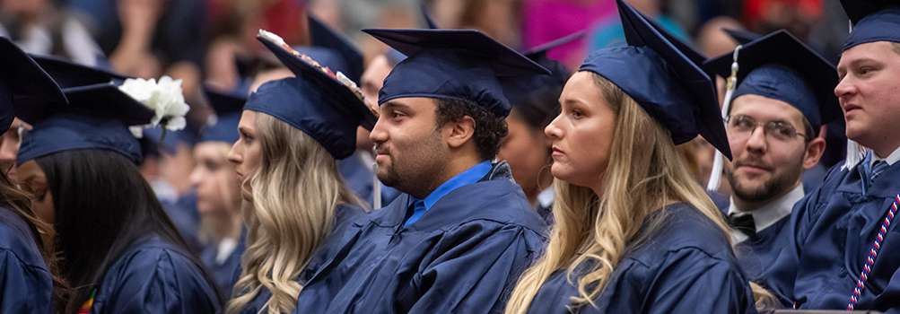 Student graduates sitting in caps and gowns at commencement ceremony