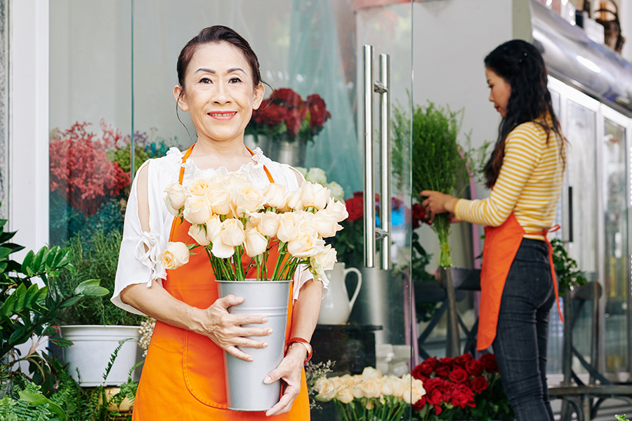 One woman holds white roses, another woman arranges flowers.