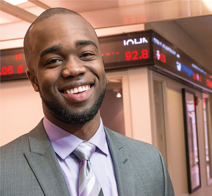 Male student wearing suit stands in front of stock ticker