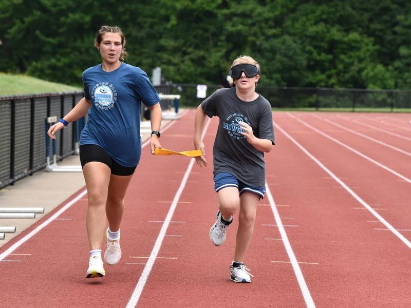 A vision-impaired athlete runs with a guide while holding a tether.