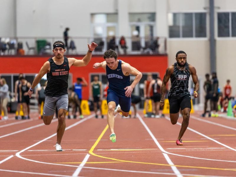 Three collegiate runners sprint to the finish line during a race.