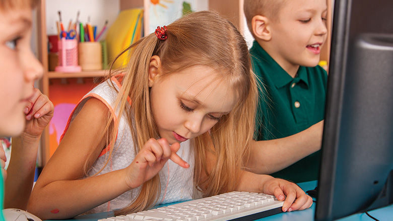 Elementary-aged students type on a computer keyboard.