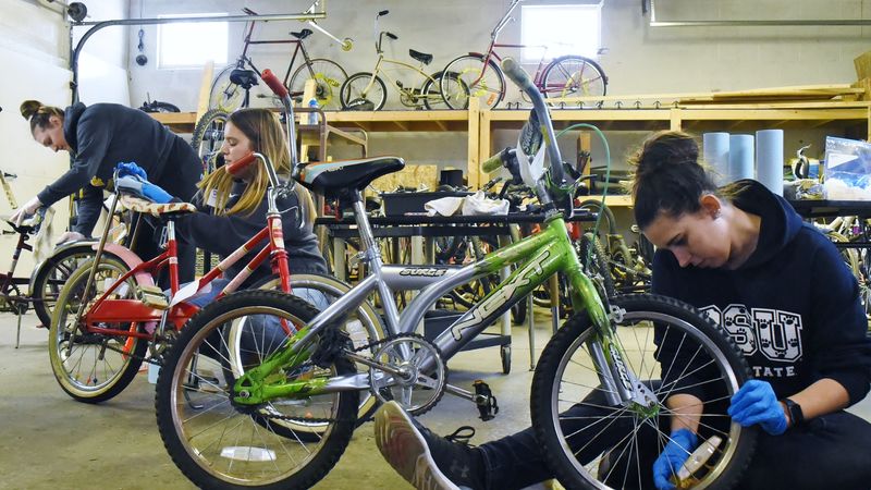Three Penn State students repair bicycles at the Sisters of St. Joseph Neighborhood Network bike warehouse.