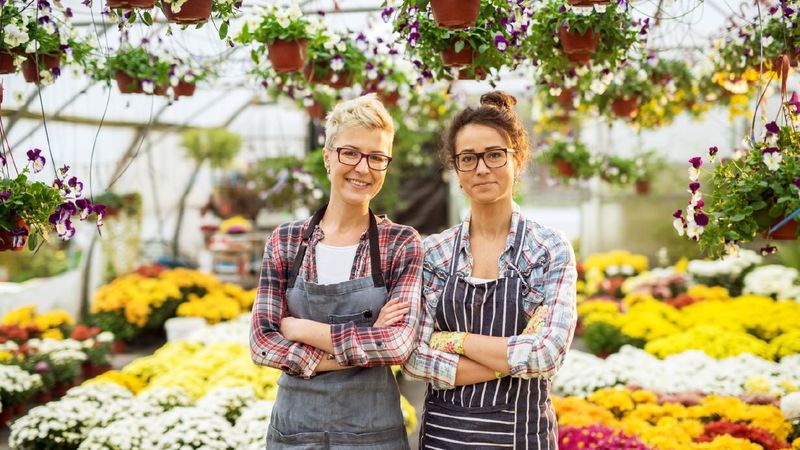 Two women pose in a floral-shop greenhouse