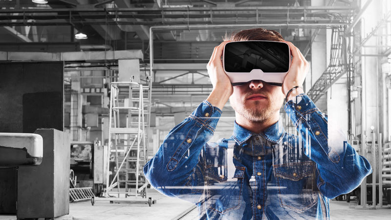 A man in an industrial setting looks through a virtual-reality headset.