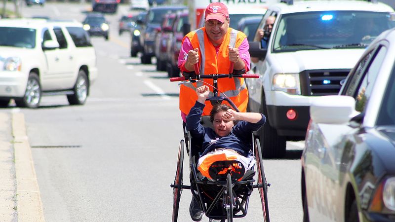 Dan Perritano pushes his daughter in a wheelchair on the side of a road.