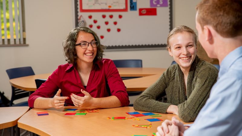 Three Penn State Behrend students talk while sitting at a classroom table.