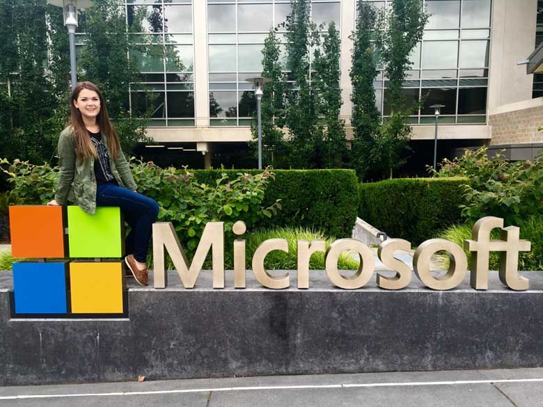 A Penn State Behrend student visits the Microsoft offices, stopping to pose for a photograph on a sign of the Microsoft logo.