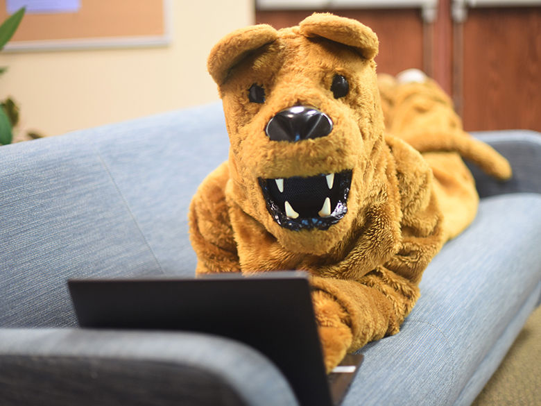 Behrend Lion mascot looks at laptop on sofa