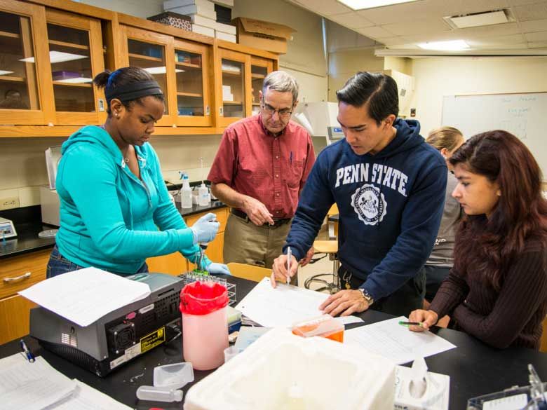 Three Penn State Behrend students learn from a professor in a science lab.