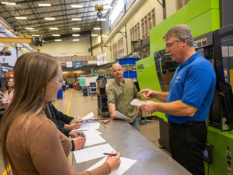 A group of students in a training session inside a plastics laboratory, led by an instructor, standing next to an ENGEL injection molding machine.