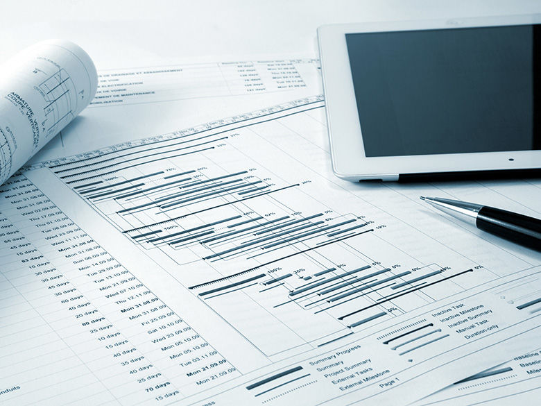 Close-up of project management documents featuring Gantt charts with timelines and tasks, placed on a desk alongside a tablet and a pen.