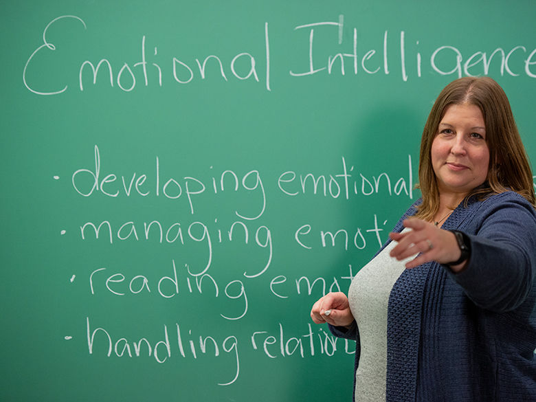 Dr. Melanie D. Hetzel-Riggin points toward her class from a chalkboard with writing on it.