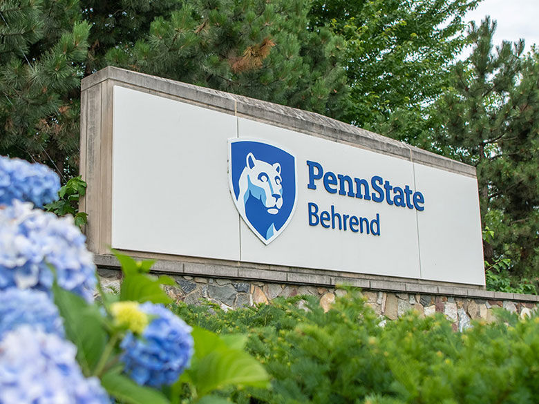 Penn State Behrend entrance sign flanked on left by blue hydrangea flowers