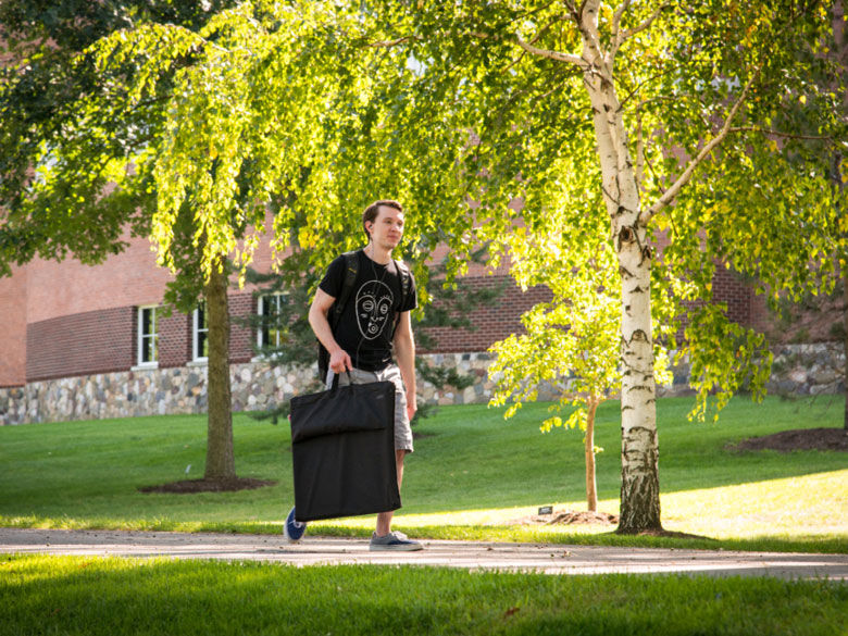 Penn State Behrend student walks across campus carrying an art portfolio.