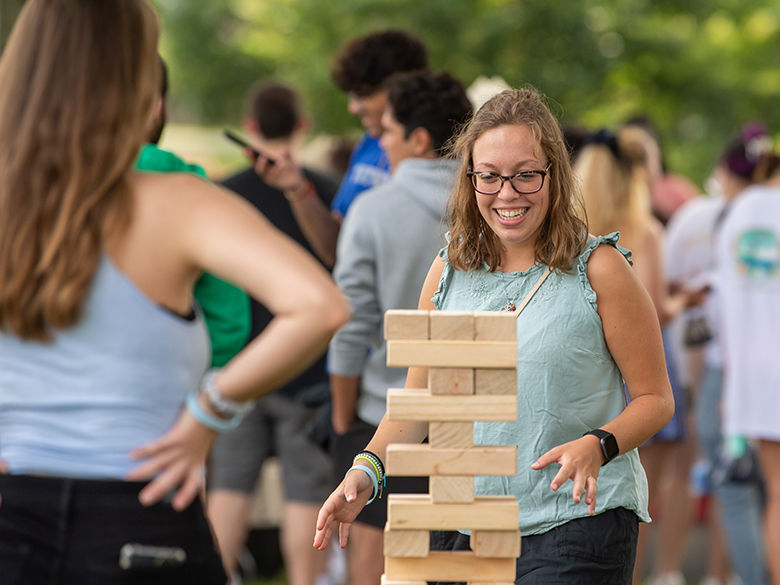 A female student smiles while playing a Jenga-style game outside.