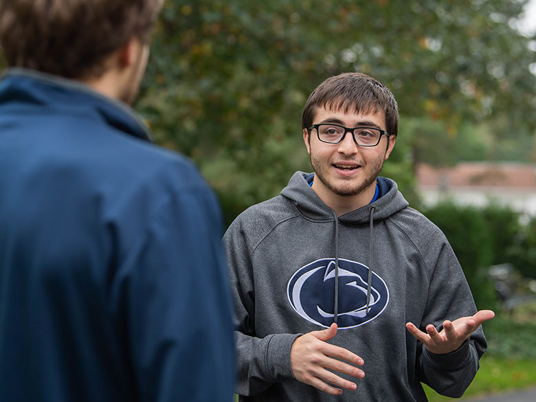 A student wearing a Penn State sweatshirt speaking to a visitor on campus