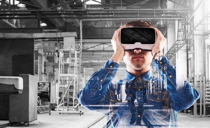 A man in an industrial setting looks through a virtual-reality headset.