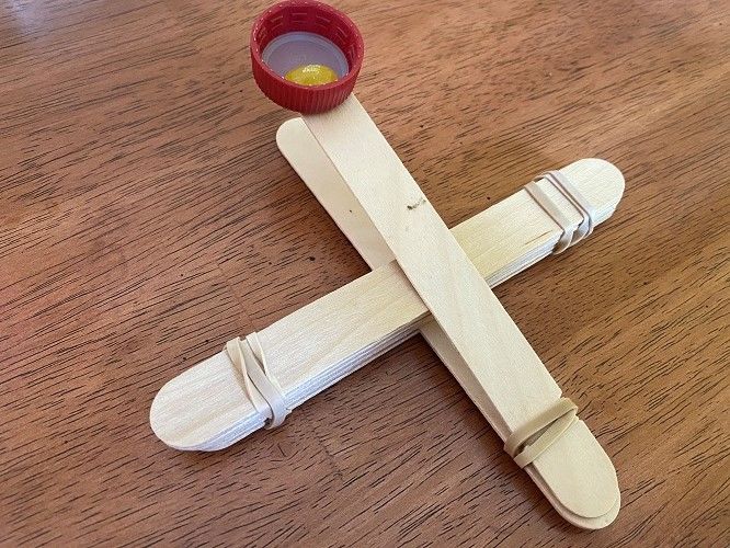 Catapult built with popsicle sticks, rubber bands, and bottle cap