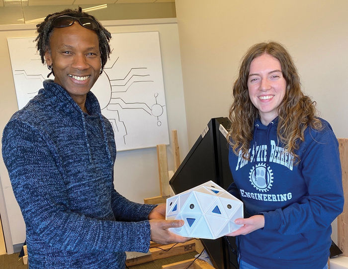 Daryl Branford, director of Science-Art Initiatives at Penn State’s Huck Institutes of the Life Sciences, left, and Alison Huffman, a 2022 Computer Engineering graduate with a minor in Music Technology, hold part of a 3-D printed icosahedral-shaped structure that Huffman designed to help illustrate virus data.