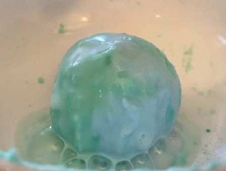Blue and green ball of baking soda mixture fizzing.