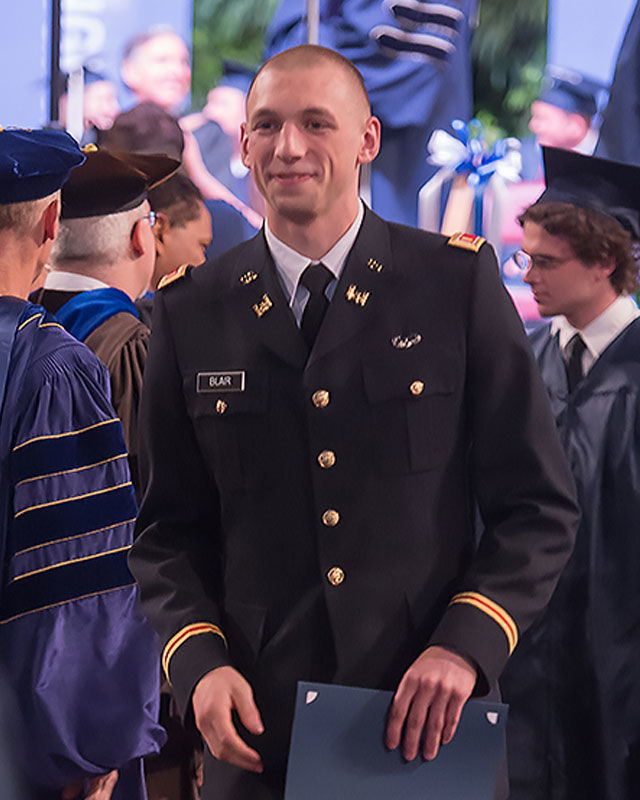 Male graduate wearing Army uniform holds diploma folder.