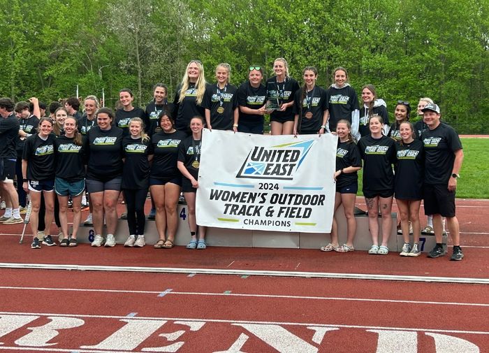 The Penn State Behrend women's track and field team celebrates with the United East championship banner.