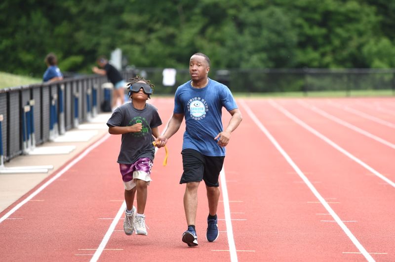 A vision-impaired athlete runs with a guide while holding a tether.